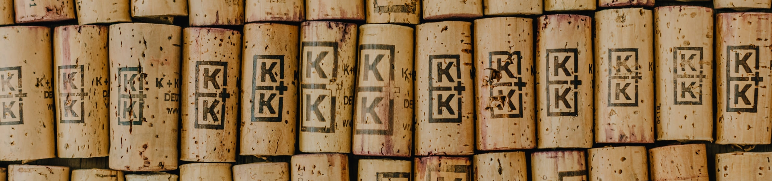 Nahaufnahme mehrerer aufrecht stehender, zusammengepresster Weinkorken, die jeweils mit „K+K“ gestempelt sind. Die Korken weisen unterschiedliche Weinflecken und Texturen auf.